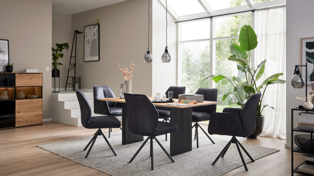 Esszimmer mit Interliving Stühlen der Serie 5116 in Schwarz, moderner Esstisch aus Holz, stilvolle Einrichtung bei Möbel Homann mit Tageslicht und Pflanzen im Hintergrund.