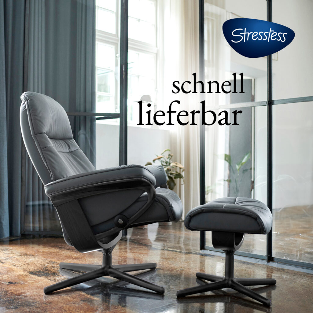 Ein schwarzer Stressless-Relaxsessel mit passendem Hocker steht in einem modern eingerichteten, lichtdurchfluteten Raum mit großen Fenstern und Vorhängen. Auf dem Bild ist das Stressless-Logo zu sehen sowie der Schriftzug „schnell lieferbar