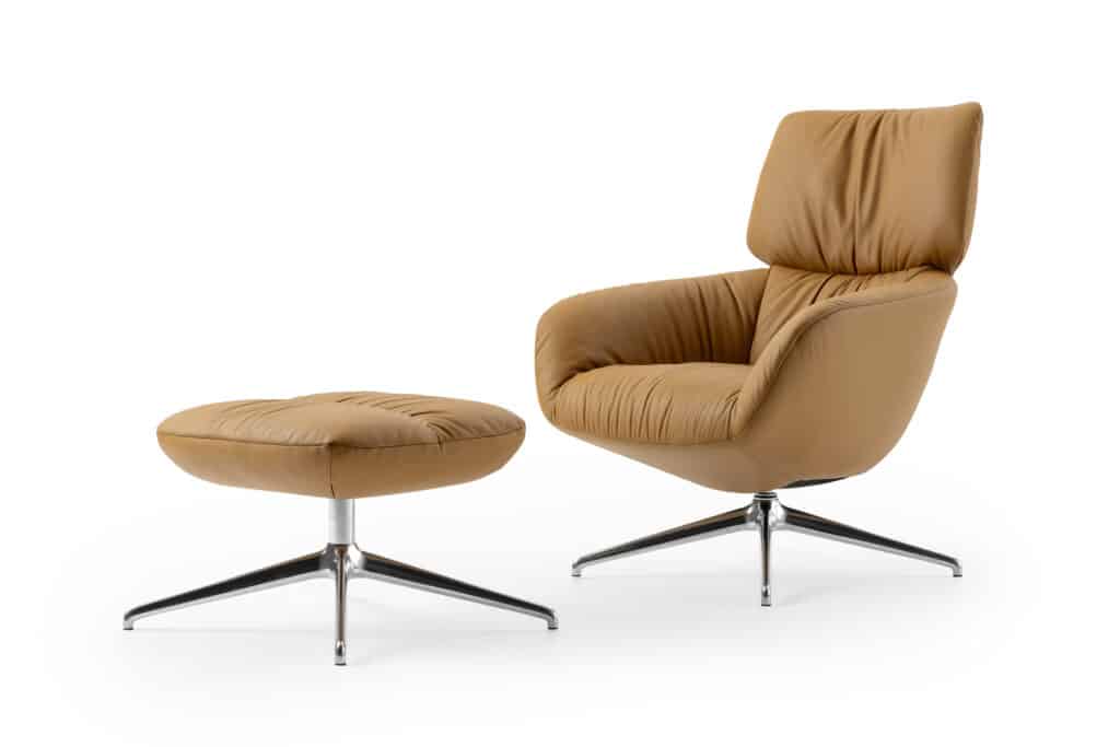 Ein moderner, beigefarbener Sessel mit passendem Hocker. Beide Möbelstücke haben ein elegantes Design mit glatten, gepolsterten Oberflächen und stehen auf einem glänzenden Metallgestell mit vier Beinen. Der Sessel verfügt über eine hohe Rückenlehne und Armlehnen für zusätzlichen Komfort, während der Hocker die Möglichkeit bietet, die Füße zu entspannen. Ein stilvolles und gemütliches Möbelset für Wohn- oder Büroräume