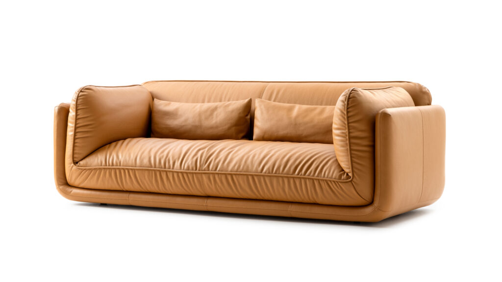 Modernes, elegantes Ledersofa in warmem Cognac-Ton mit weichen, abgerundeten Formen und zwei passenden Rückenkissen. Das Design wirkt einladend und luxuriös, ideal für stilvolle Wohnräume