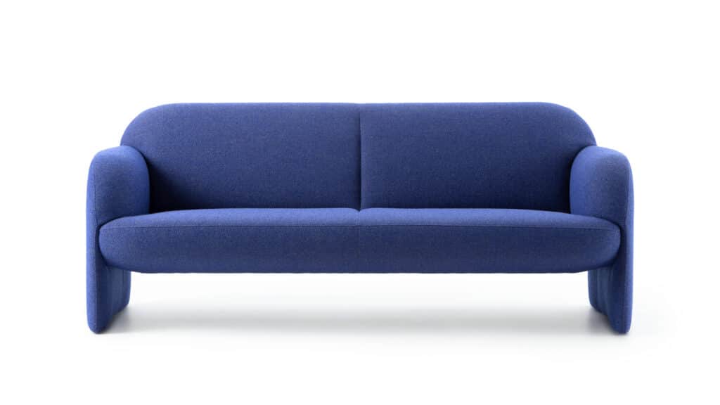 Ein modernes Sofa in kräftigem Blau mit abgerundeter Form, gepolsterten Armlehnen und einer durchgehenden Sitzfläche. Die Rückenlehne ist zweigeteilt und durch eine Naht verbunden. Das Sofa steht auf breiten, gepolsterten Beinen, die in Farbe und Textur mit dem Rest des Sofas übereinstimmen