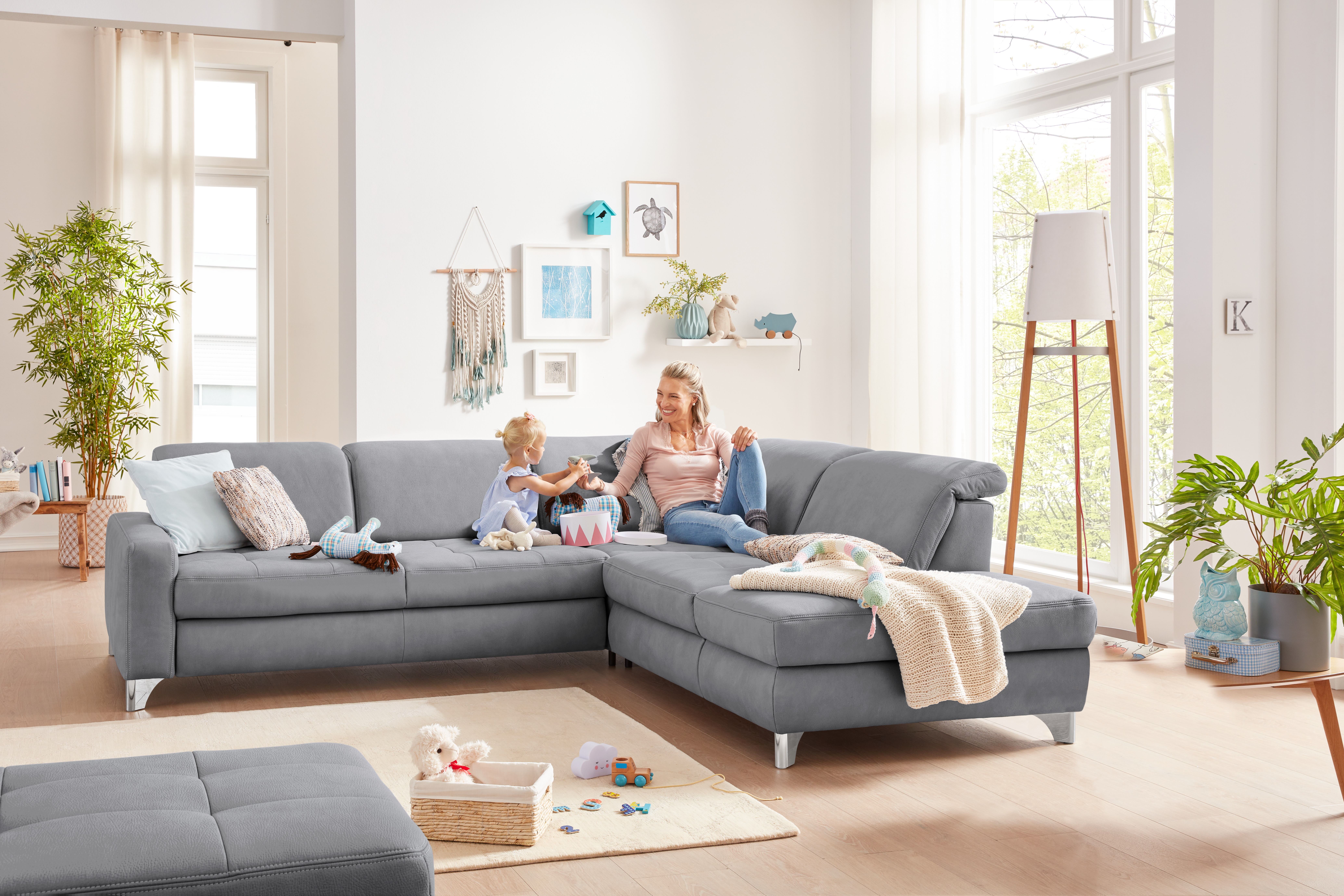 Hell graues Ecksofa mit Mutter und Kind in einem hellen Lichtdurchfluteten Raum