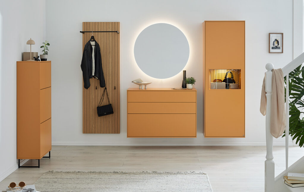 Modernes Eingangsbereich-Design mit warmen Orangetönen: Spiegel mit indirekter Beleuchtung, schwebende Kommoden, Design-Lampe und Pflanzen inszenieren ein harmonisches, wohnliches Ambiente – stilvolles Interior mit Herz.