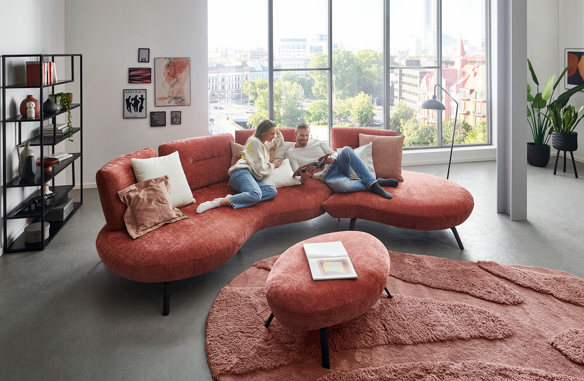 Ein Sofa ohne ecken in der Farbe Himbeere. Ein Designsofa auf dem ein Pärchen zusammen sitzt.