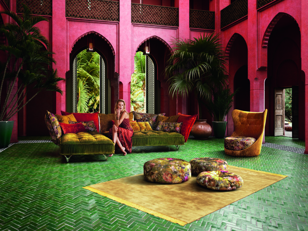 Wohnzimmer im marokkanischen Stil mit roten Wänden, grüner Samtcouch, gelbem Teppich, floralen Sitzhockern und tropischen Pflanzen – farbenfrohes, luxuriöses Interior mit orientalischen Akzenten.