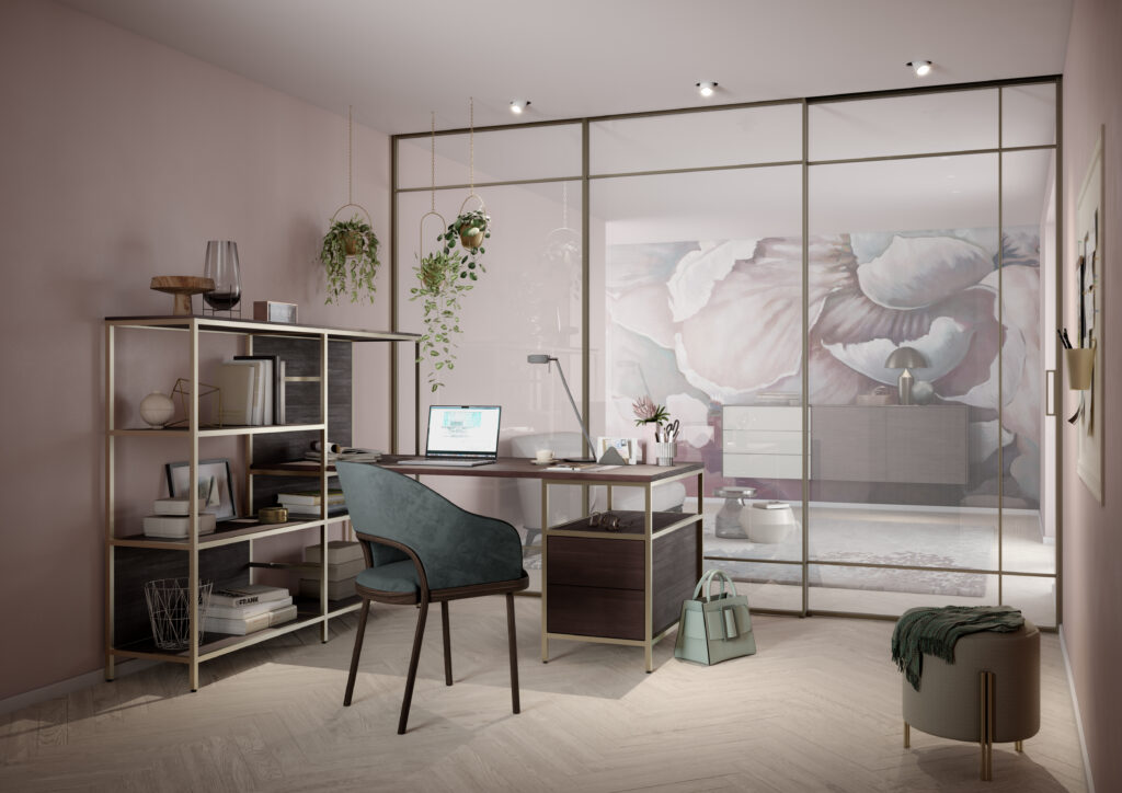 Ein stilvoll eingerichtetes Homeoffice mit modernem Flair. Im Mittelpunkt steht ein Schreibtisch mit Laptop, Lampe, Schreibutensilien und einer Tasse. Davor befindet sich ein komfortabler Bürostuhl. Links neben dem Tisch steht ein Regal mit Büchern, Dekoration und Aufbewahrungsboxen. Über dem Arbeitsplatz hängen drei grüne Pflanzen. Der Raum wird durch eine Glas-Schiebetür vom angrenzenden Bereich mit einer auffälligen Blumenmuster-Wand getrennt. Auf dem Boden liegt ein kleiner Hocker mit einer grünen Decke und einer passenden Handtasche. Der Boden ist aus hellem Holz, die Wände sind in einem sanften Rosaton gestrichen. Die Beleuchtung erfolgt über eingelassene Deckenstrahler.