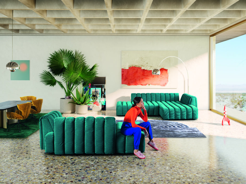 Modernes Wohnzimmer mit modularer türkisfarbener L-förmiger Couch, gestreiftem Teppich, großem Zimmerpflanze, abstrakter Wandkunst und Blick auf eine Wüstenlandschaft – stilvolle Einrichtung mit verspielten Details wie einer Spielzeugrakete und einem Essbereich mit senfgelben Stühlen.