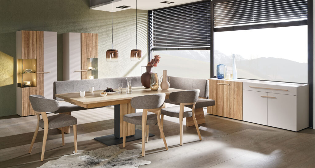 Helles Esszimmer mit Holz-Esstisch, grauen Polsterstühlen und Eckbank; warme Pendelleuchten und dekorative Möbel in skandinavischem Design.