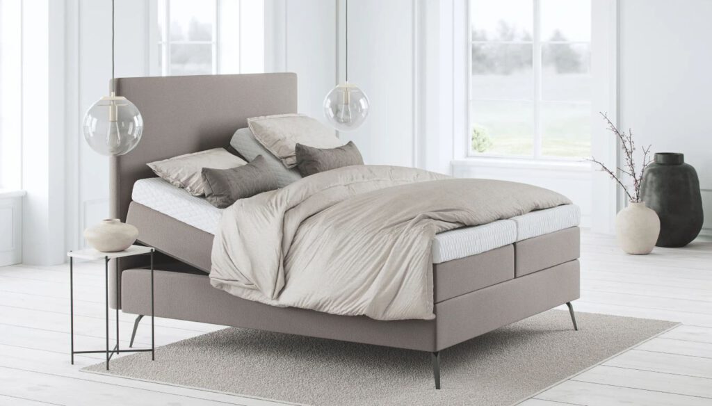 Modernes Schlafzimmer mit verstellbarem Bett, beiger Bettwäsche, Pendelleuchten, großen Fenstern mit Blick ins Grüne und stilvoller, heller Einrichtung.