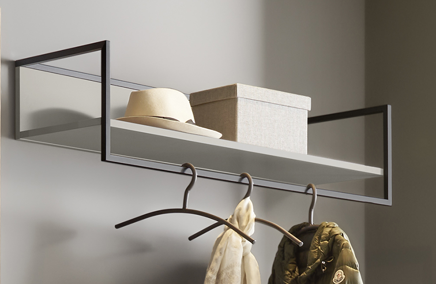 Wandmontiertes Regal mit minimalistischer Gestaltung, bestehend aus einem schwarzen Metallrahmen und einer hellen Ablagefläche. Auf dem Regal liegen ein beigefarbener Hut und eine rechteckige, stoffbezogene Aufbewahrungsbox. Darunter hängen zwei Kleiderbügel – einer mit einem hellen Schal, der andere mit einer grünen Jacke. Die Szene zeigt eine stilvolle und praktische Lösung zur ordentlichen Aufbewahrung von Kleidung und Accessoires.