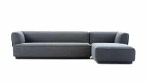 Modernes Ecksofa in grauem Stoff mit klaren Linien und niedriger Silhouette – bestehend aus langer Sitzfläche und seitlicher Chaiselongue, ideal für zeitgemäße Wohnräume.