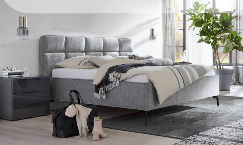 Modernes Schlafzimmer mit grauem Polsterbett, stilvollen Pendelleuchten und gemütlicher Deko – elegantes Design trifft auf wohnliche Atmosphäre.