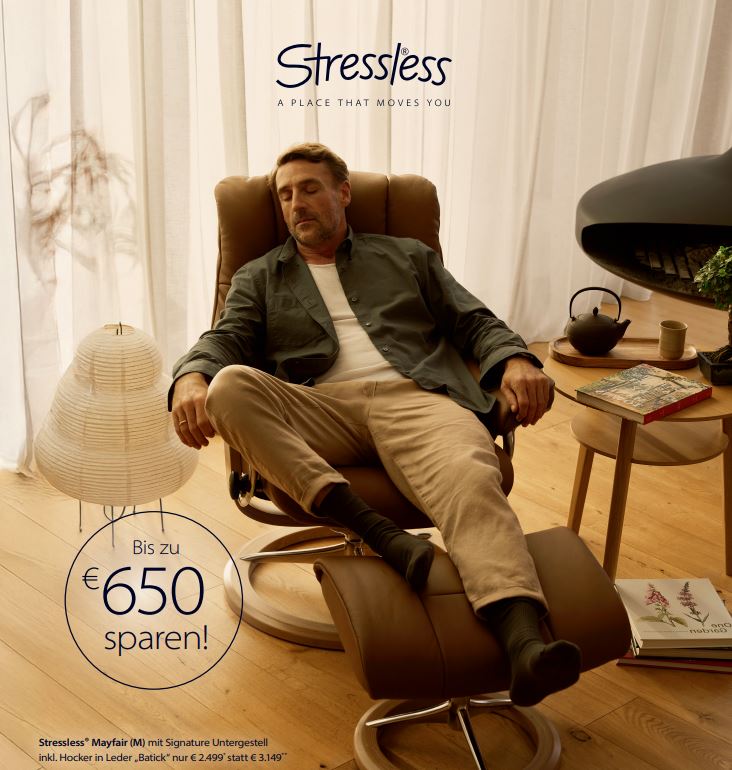 Ein Mann entspannt in einem braunen Leder-Relaxsessel mit passendem Hocker der Marke Stressless® Mayfair (M) mit Signature-Untergestell. Der Sessel steht in einem gemütlich eingerichteten, hellen Raum mit Holzfußboden, einem kleinen Beistelltisch mit Tasse und Buch, einer modernen Stehlampe und einer Zimmerpflanze im Hintergrund. Werbetext im Bild weist auf einen Rabatt von bis zu 650 € hin – Aktionspreis: 2.499 € statt 3.149 €