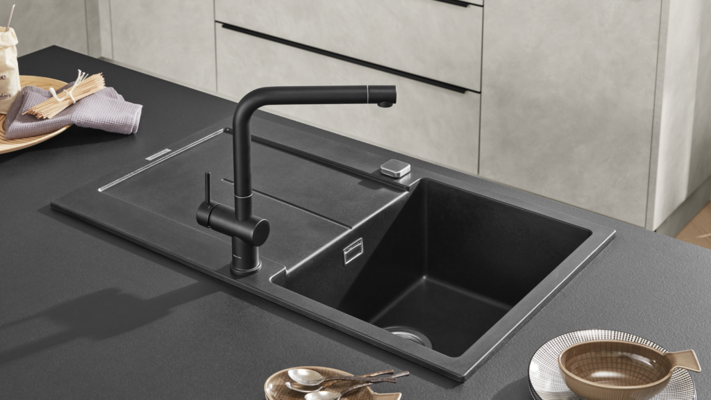 Mattschwarzer Küchenwasserhahn über integrierter Spüle, daneben Holzplatte mit Mehl, Spaghetti und Geschirr. Moderne Küche mit hellen Fronten und klarer Linienführung