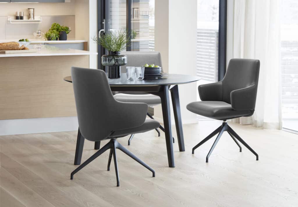 Grauer Stressless Laurel Esszimmerstuhl mit Armlehnen an einem hellen Esstisch.