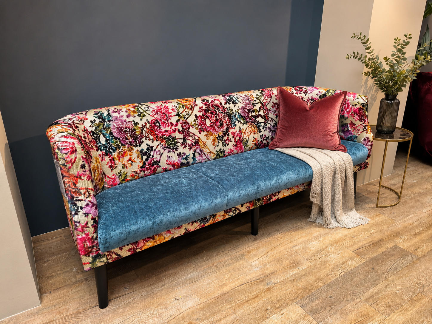 Exklusives Designer-Sofa mit buntem Blumenmuster und blauer Sitzfläche, stilvoll dekoriert im neuen Möbel Homann Designstudio.