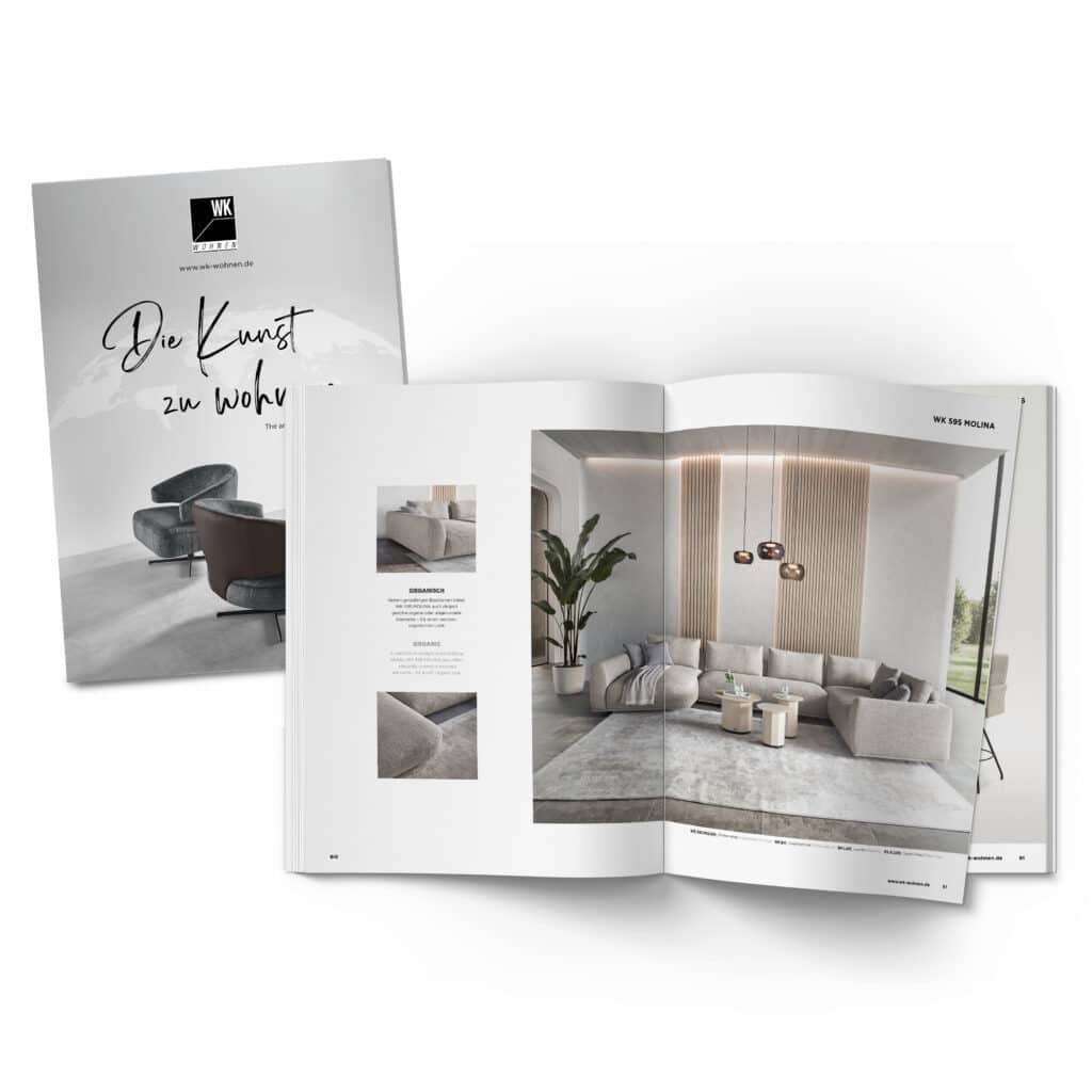 Offenes Wohnmagazin auf weißem Untergrund, das eine moderne Wohnzimmerszene mit großem Ecksofa, Couchtischen, Pflanzen und bodentiefen Fenstern zeigt. Daneben liegt ein geschlossenes Magazin mit dem Titel „Die Kunst zu Wohnen