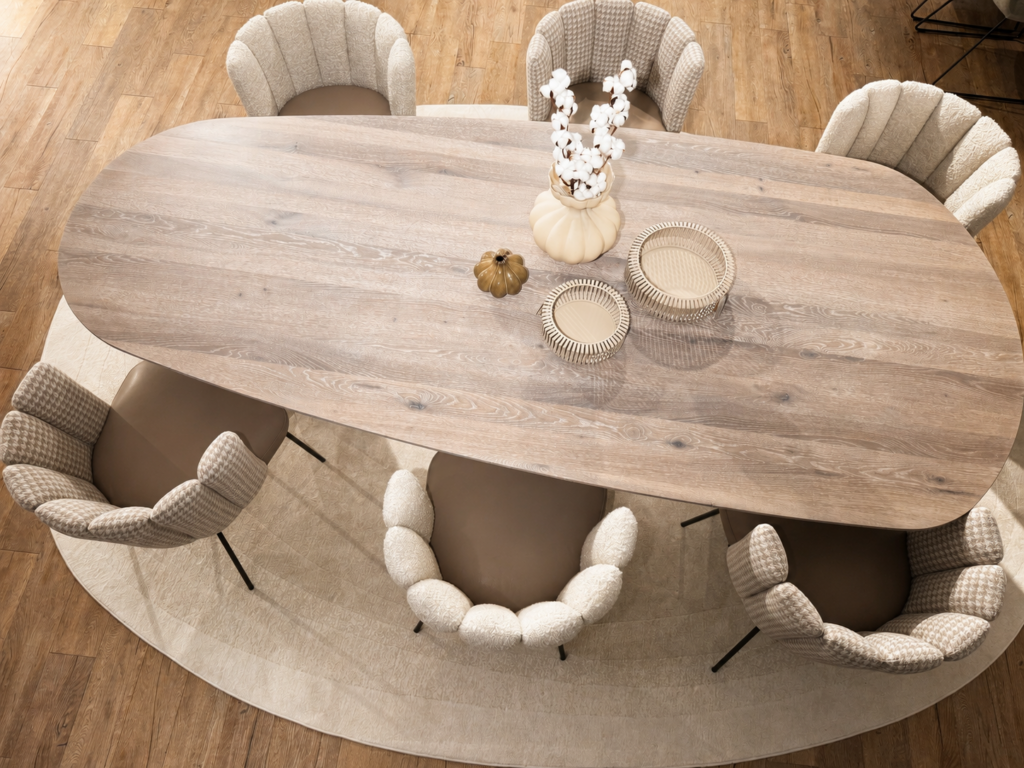 Elegantes KFF Esszimmer-Set mit einem großen ovalen Asco Holztisch, umgeben von sieben verschiedenen Polsterstühlen aus strukturiertem Stoff und Leder. Die Gruppe steht auf einem strukturierten runden Teppich auf Holzboden vor einer warmen Wand mit beleuchteter Nische.